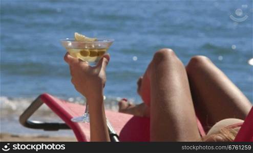 Female hand holding martini cocktail with olives on tropical beach