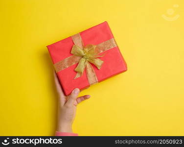 female hand holding red gift box on a yellow background, concept of congratulations on birthday