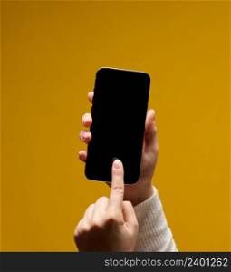 female hand holding smartphone with blank black screen on yellow background