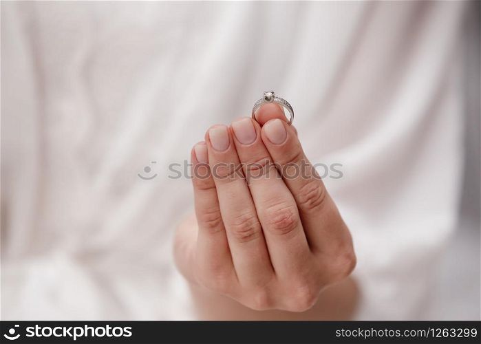 female hand holding wedding ring made of white gold and diamonds on a white background. Luxury expensive proposal ring. Bride in wedding day. female hand holding wedding ring made of white gold and diamonds on a white background. Luxury expensive proposal ring. Bride in wedding day.