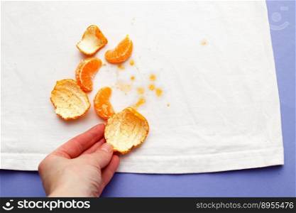 female hand holding white clothes with ditry stains from fruits mandarin on purple very peri background.. female hand holding white clothes with ditry stains from fruits mandarin on purple very peri background