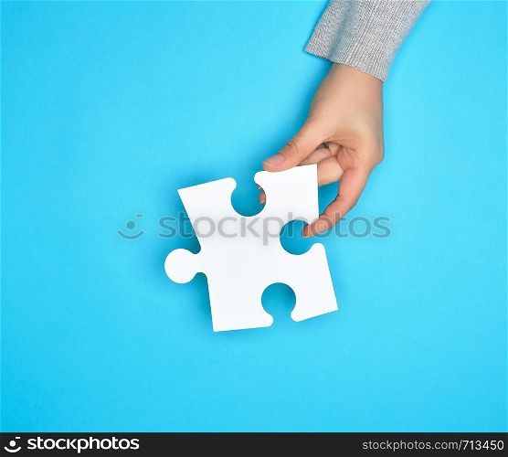 female hand holding white empty paper puzzle, blue background, copy space