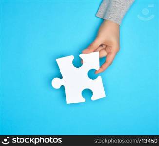 female hand holding white empty paper puzzle, blue background, copy space