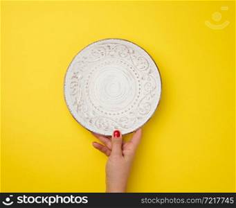 female hand holding white empty round plate on a yellow background, top view