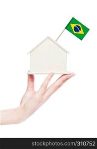 Female hand holding wooden house model with Brazil flag on top.