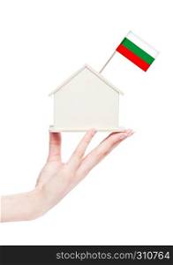 Female hand holding wooden house model with Bulgaria flag on top.
