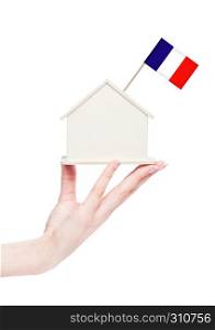 Female hand holding wooden house model with France flag on top.