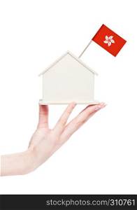 Female hand holding wooden house model with Hong Kong flag on top.