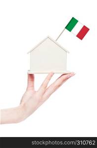 Female hand holding wooden house model with Italy flag on top.