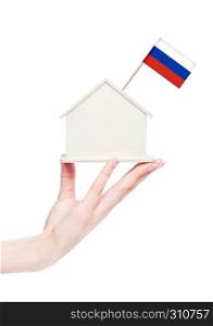 Female hand holding wooden house model with Russia flag on top.