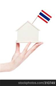 Female hand holding wooden house model with Thailand flag on top