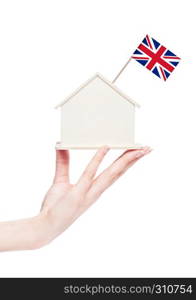 Female hand holding wooden house model with United Kingdom flag on top.