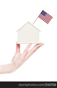 Female hand holding wooden house model with United States of America flag on top.