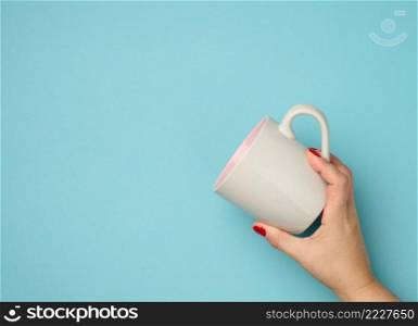female hand holds a ceramic mug on a blue background, break time and drink coffee, copy space