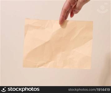 female hand holds a crumpled sheet of paper on a beige background. Place for inscriptions and announcements