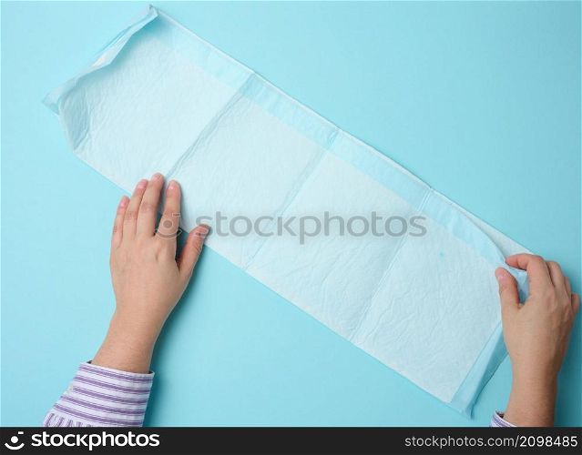 female hand holds a disposable medical diaper on a blue background. Hygiene product