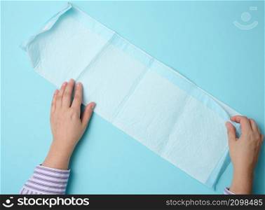 female hand holds a disposable medical diaper on a blue background. Hygiene product
