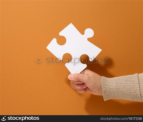 female hand holds a fragment of a white large puzzle on a brown background, the concept of finding an idea, solving a problem