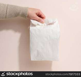 female hand holds a full paper bag on a beige background. Refusal from plastic packaging, food delivery