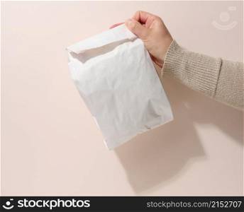 female hand holds a full paper bag on a beige background. Refusal from plastic packaging, food delivery