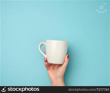female hand holds a gray ceramic mug on a blue background, break time and drink coffee