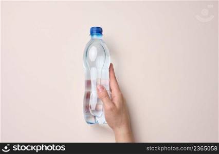 female hand holds a plastic transparent bottle on a beige background