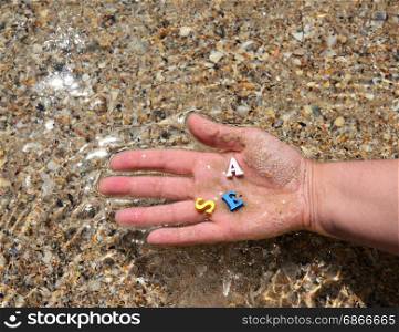 Female hand holds a wooden letter on the background of the sea with a smooth surface