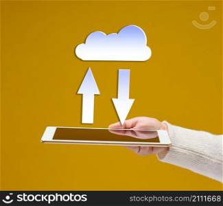 female hand holds an electronic gadget tablet on a yellow background, white cloud with arrows above it. Information exchange, data warehouse. Uploading a backup