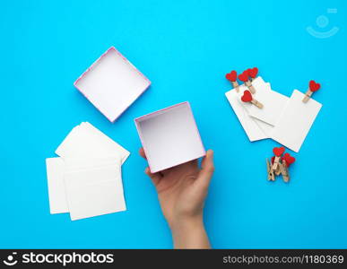 female hand holds an empty open square box on a blue background, top view, concept of giving gifts