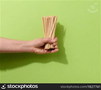 female hand holds disposable wooden sticks for stirring hot drinks on a green background. Coffee and tea spoon, zero waste