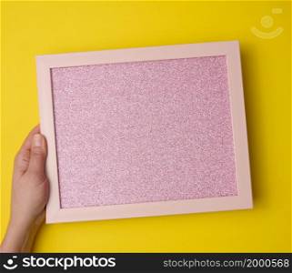 female hand holds empty pink frame on yellow background. Place for inscription