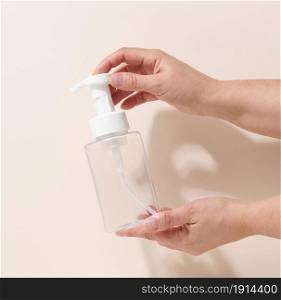 female hand holds empty plastic container with dispenser for liquid products, soap or shampoo on beige background