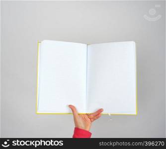 female hand holds open yellow notepad into a cell on gray background, copy space