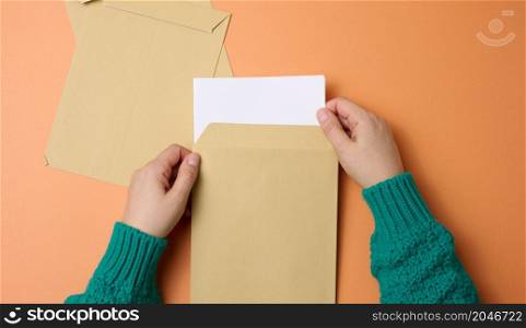female hand holds paper envelopes on an orange background, top view. Correspondence
