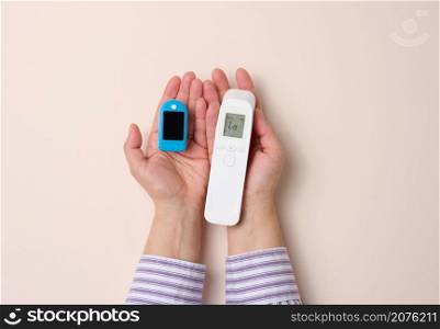 female hand holds plastic non-contact thermometer and oximeter on beige background