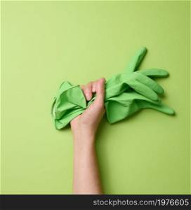 female hand holds rubber green gloves for cleaning on a green background. Part of the body is lifted up