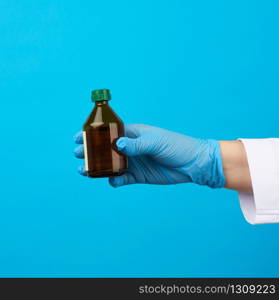 female hand in blue latex medical glove holds a brown glass bottle for medicines, blue background