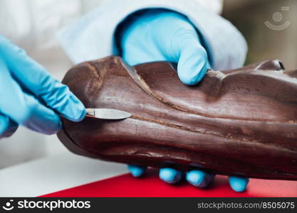 Female hand in protective gloves preparing area of wooden sculpture for restoration. Preparing Area of Wooden Sculpture for Restoration 