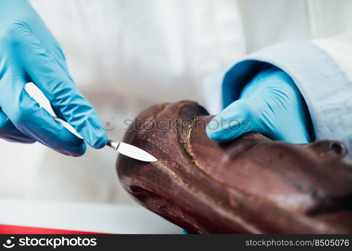 Female hand in protective gloves preparing area of wooden sculpture for restoration. Preparing Area of Wooden Sculpture for Restoration 