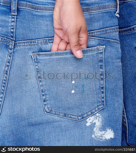 female hand is stuck in the back pocket of blue jeans, close up, full frame