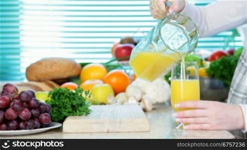 Female hand pouring orange juice in the kitchen near a lot of vegetables and fruits