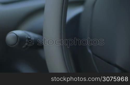 Female hand pushing sound audio control buttons on the left hand side on the steering wheel of modern car while driving
