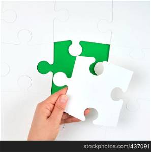 female hand puts empty white big puzzles on a green background, one element missing, top view