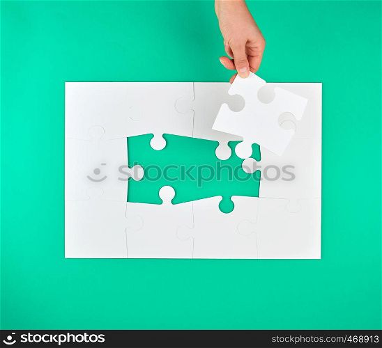 female hand puts empty white big puzzles on a green background, top view