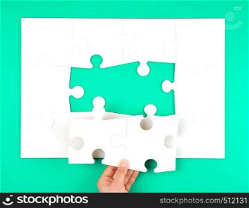 female hand puts empty white big puzzles on a green background, two elements missing, top view