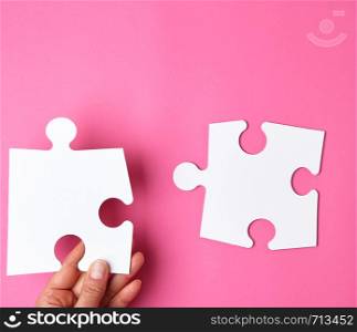 female hand puts white big empty puzzles on a pink background, top view