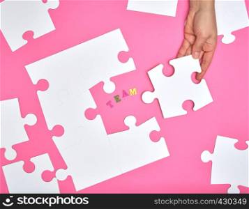 female hand puts white big puzzles on a pink background, inscription team. concept of recruitment in the company