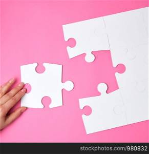 female hand puts white big puzzles on a pink background, one element missing, top view