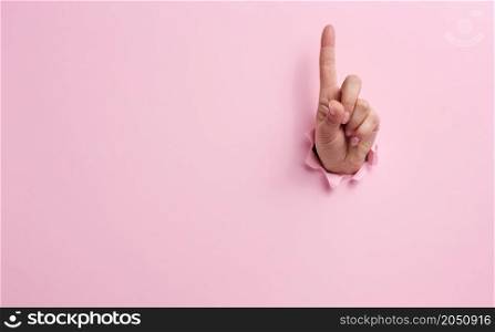 female hand sticking out of a torn hole in a pink paper background, attention gesture. Place for an inscription