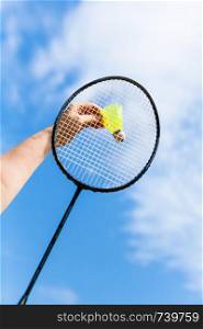 female hand strikes yellow shuttlecock by badminton racquet with background from blue sky with white clouds in sunny day (focus on the shuttlecock)